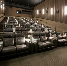 an empty auditorium with rows of recliners in front of the seats and lights on the wall