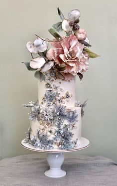 a three tiered cake decorated with flowers and greenery on a tablecloth covered surface