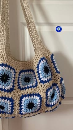 a crocheted purse hanging from a hook on a white door with blue accents