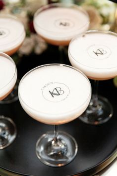 four martinis sitting on top of a black tray with flowers in the back ground