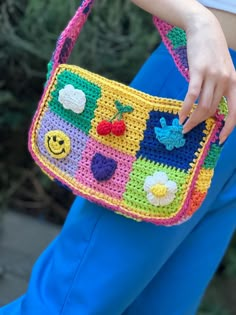 a woman is holding a crocheted purse in her left hand and wearing blue pants