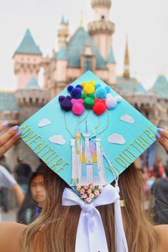 a woman wearing a blue graduation cap with colorful balloons on it's head in front of a castle