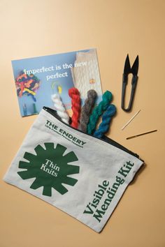 scissors, yarn, and needle tips are on the table next to a bag with an advertisement