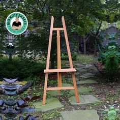 a wooden easel sitting in the middle of a garden next to a stone path