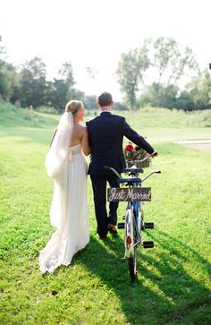 a bride and groom walking their bike in the grass