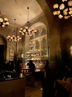 a group of people standing around a bar with lights hanging from it's ceiling