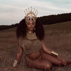 a woman in a golden outfit sitting on the ground with her legs crossed and wearing a crown