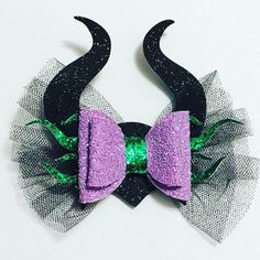 two horns with purple and green sequins are attached to black tulle on a white surface