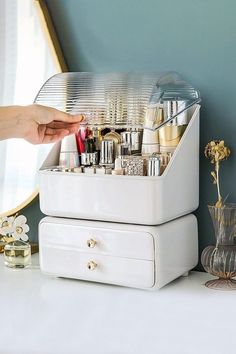 a person is holding their hand over the top of a white container filled with cosmetics