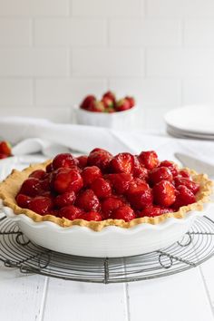 there is a pie with strawberries in it on the cooling rack next to plates