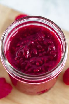 a jar filled with raspberry jam sitting on top of a wooden cutting board