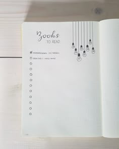 an open notebook with the words books to read written on it and hanging from strings