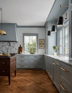 a large kitchen with wood floors and gray cabinets, marble counter tops and gold accents