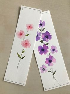 two bookmarks with watercolor flowers painted on them, one is pink and the other is purple