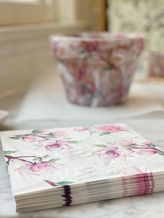 a stack of pink flowers sitting on top of a table next to a flower pot