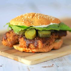 a chicken burger with lettuce and pickles on a cutting board