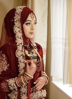 a woman in a red and gold bridal outfit standing next to a window with her hands on her hips