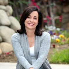 a woman sitting on the ground with her legs crossed and looking at the camera smiling