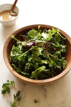 a wooden bowl filled with lettuce next to a cup of soup