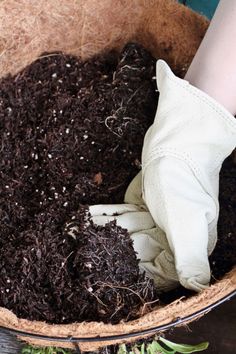 someone is digging dirt in a basket with gardening gloves