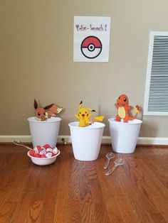 three plastic cups with pokemon figurines in them on a wooden floor next to a wall