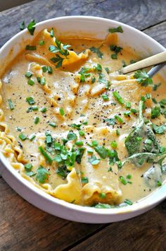 a white bowl filled with pasta and cheese on top of a wooden table next to a spoon