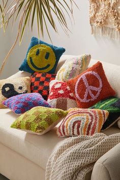 colorful pillows are arranged on a couch in front of a potted plant and wall hanging