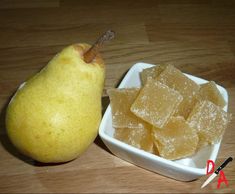 a small white bowl filled with sugar next to a yellow pear on a wooden table