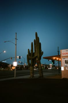 a giant cactus sculpture in front of a gas station at night with the sun going down