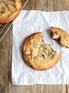 two chocolate chip cookies sitting on top of a piece of paper next to a cooling rack