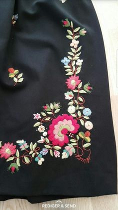 an embroidered black fabric with flowers and leaves on the side, sitting on top of a wooden floor