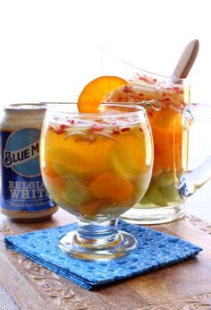 two glasses filled with water and fruit on top of a wooden table next to cans