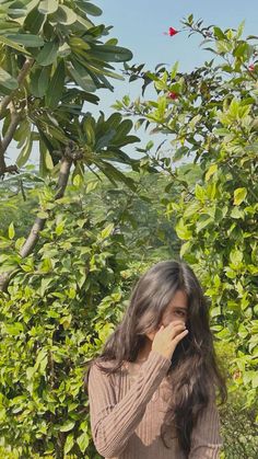 a woman standing in front of trees talking on her cell phone