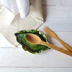 two wooden spoons and a green leaf shaped bowl on a white table with towels