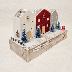 a small wooden box with houses and trees on it in the middle of snow covered ground