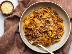 a white bowl filled with pasta and meat on top of a brown cloth next to a spoon