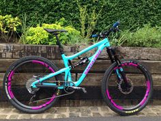 a blue and pink mountain bike parked on the side of a wooden fence next to flowers