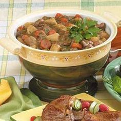 a table topped with plates of food and bowls of vegetables on top of it, next to a bowl of stew