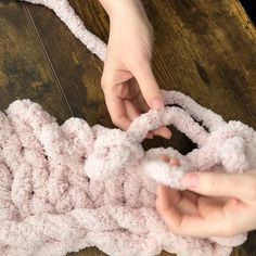 two hands crocheting the ends of a pink blanket on a wooden table top