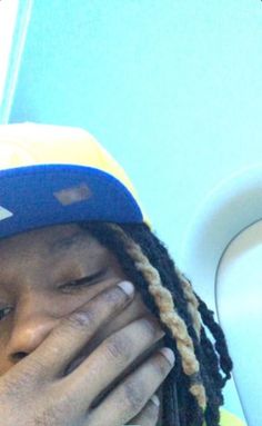 a man with dreadlocks covers his face as he sits on an airplane seat