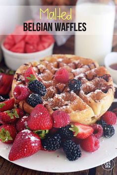 a waffle topped with berries and strawberries on a plate next to a glass of milk