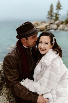 a man and woman in winter clothes embracing each other by the water's edge