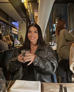 a woman sitting at a table with a glass in her hand and smiling for the camera