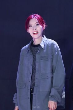 a woman with red hair standing in front of a black background wearing a gray shirt