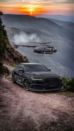 two cars parked on the side of a dirt road next to a helicopter flying above