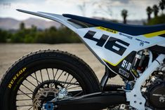 a white and yellow dirt bike parked on top of a gravel road next to trees