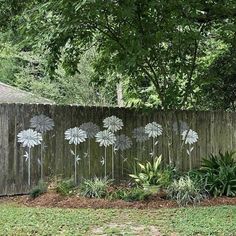 a fence with flowers painted on it next to grass and trees in the back yard