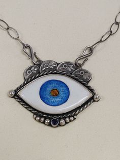 Handmade from scratch Evil Eye Hamsa Cloisonne Enamel Necklace   Handmade by me in my beautiful Kansas City studio. See our work and follow us on Instagram please. Questions and comments are welcome.  Instagram: https://www.instagram.com/anaraandco/ Sterling Silver and Fine Silver necklace is made in glass vitreous Japanese enamel. Setting made out of sterling silver. Front adorned with silver balls, hand stamped design on top, sapphire stone is set in bezel setting, back has a hand sewn hamsa hand. All cut by hand. Soldered, stamped, handsewn, grinded, polished, oxidized.  Vitreous enamel, also called porcelain enamel, it's when material made by fusing powdered glass to a substrate by firing. The powder melts in the special kiln at 1500 degree F, flows, and then hardens to a smooth, durab Evil Eye Hamsa, Vitreous Enamel, Enamel Necklaces, Cloisonne Enamel, Evil Eye Necklace, Sapphire Stone, Hamsa Hand, Stamp Design, Eye Necklace