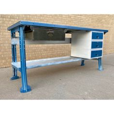 a blue and white desk with drawers in front of a brick wall