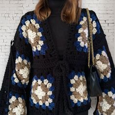 a woman wearing a black sweater with blue, white and brown crocheted flowers